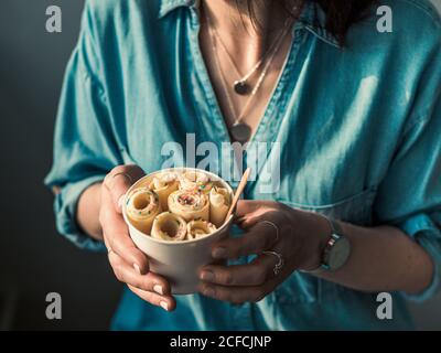 Gelato arrotolato in tazza conica in mani Donna. Donna in jeans camicia contiene cono tazza con vaniglia stile tailandese laminato gelato Foto Stock