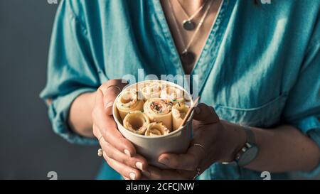 Gelato arrotolato in tazza conica in mani Donna. Donna in jeans camicia contiene cono tazza con vaniglia stile tailandese laminato gelato Foto Stock