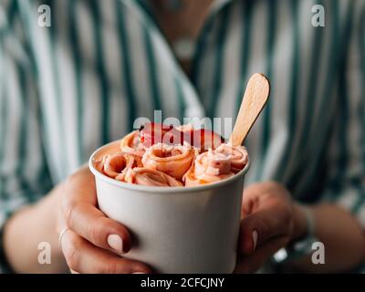 Gelato arrotolato con fragola in tazza conica in mani di Donna. Tazza conica con gelato arrotolato in stile tailandese Foto Stock