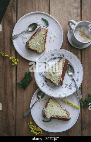 Vista dall'alto di fette di limone vegano fresco e cocco cake su piatti con cucchiai e tazza di caffè Foto Stock