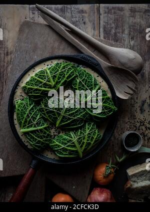 Da sopra foglie di cavolo ripieni di riso su padella vicino pagaia, cucchiaio, arance, pompelmo e fetta di pane su sfondo di legno Foto Stock
