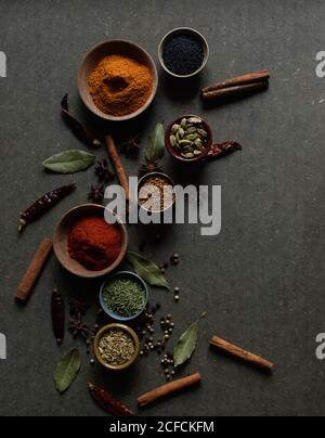 Composizione vista dall'alto con diversi tipi di spezie aromatiche naturali posizionato su sfondo grigio scuro Foto Stock
