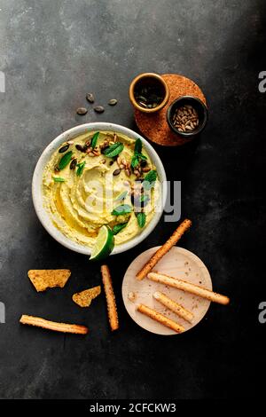 Da sopra i piselli dell'hummus messi su una ciotola vicino ai cracker su sfondo scuro Foto Stock