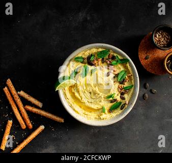 Da sopra i piselli dell'hummus messi su una ciotola vicino ai cracker su sfondo scuro Foto Stock