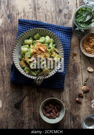 Da sopra ciotola di pasta appetitosa paccheri con kale fresco pesto e arachidi macinate su tavola in legno Foto Stock