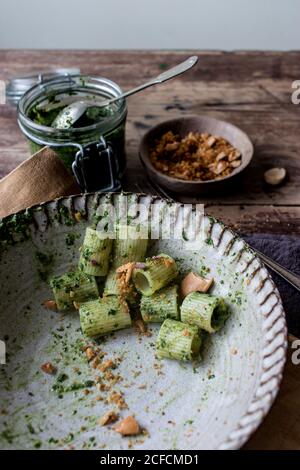 Da sopra ciotola di pasta appetitosa paccheri con kale fresco pesto e arachidi macinate su tavola in legno Foto Stock