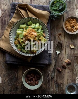 Da sopra ciotola di pasta appetitosa paccheri con kale fresco pesto e arachidi macinate su tavola in legno Foto Stock