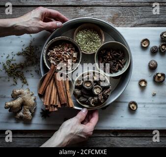 Vista dall'alto di una persona irriconoscibile che tiene le mani di spezie secche miste E funghi composti su tavola di marmo per cucinare la zuppa di Pho Foto Stock