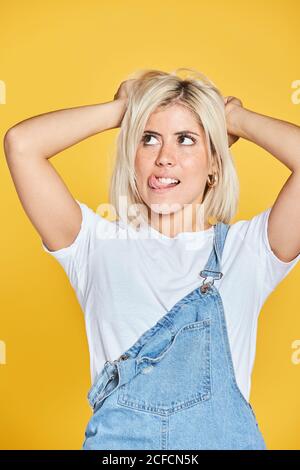 Bella giovane donna in t-shirt bianca e jeans sundress in piedi su sfondo giallo e guardando verso il basso Foto Stock