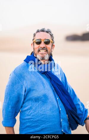 Uomo mature bearded guardando la macchina fotografica mentre camminando in sabbia Deserto contro il cielo grigio in Marocco Foto Stock