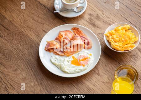 Da sopra uova fresche fritte con pancetta in piatto servita a tavola con succo di frutta e caffè per colazione Foto Stock