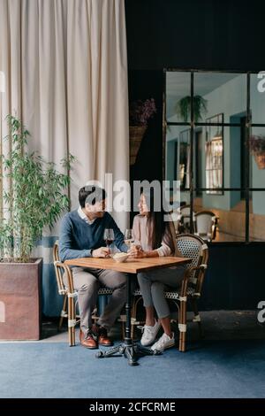 Felice giovane coppia affettuosa romantica con bicchieri di vino e. tenere le mani mentre si siede a un tavolo di legno in un'accogliente caffetteria Foto Stock