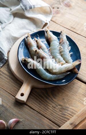 Alto angolo di grandi gamberi grigi grezzi su blu grande piastra sul tagliere su tavola rustica in legno in luce cucina Foto Stock