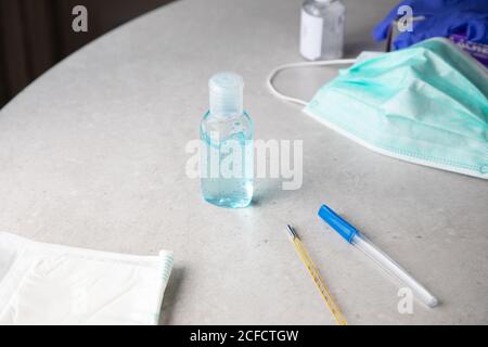 Da sopra gel antibatterico per la prevenzione del coronavirus posto sul tavolo con maschera facciale e termometro Foto Stock