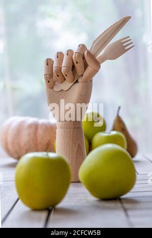 Mano di legno con coltello e forchetta posta sul tavolo con frutta fresca e verdura per una dieta nutriente Foto Stock