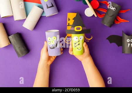 Il ragazzo fa i giocattoli di Halloween dalla carta. rotolo del water tubo dalle mani. Fai da te per i bambini su backgrpund viola tradizionale. Festa di progetto di arredamento domestico. Sala Foto Stock