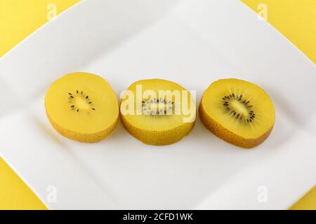 Tre fette di kiwi giallo dorato su dessert bianco piastra su sfondo giallo Foto Stock