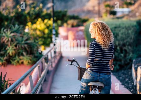 Bella donna bionda riccia vista dal retro - persone in una sana attività di giro in bicicletta nel parco cittadino - gratuito da emergenza concetto di soggiorno a casa Foto Stock