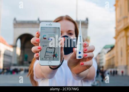 Donna dai capelli rossi con l'app di avvertimento Corona sull'iphone di Monaco Su Odeonsplatz Foto Stock