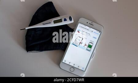 Applicazione di avvertenza Corona sull'iphone e maschera al naso sul tavolo con termometro clinico Foto Stock