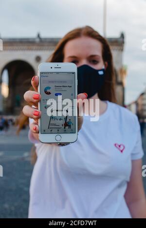 Donna dai capelli rossi con l'app di avvertimento Corona sull'iphone di Monaco Su Odeonsplatz Foto Stock