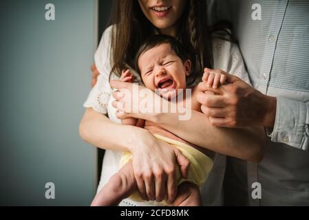 anonimo uomo e donna abbracciando e confortando bambino neonato piangente in stanza accogliente a casa Foto Stock