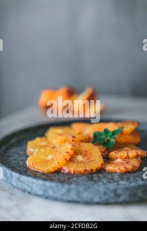 Vista dall'alto di fette di agrumi freschi disposte su un piatto con buccia d'arancia e posto sul tavolo in cucina Foto Stock