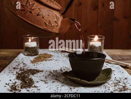 Serve tè saporito e fragrante in tazza di teiera in argilla e dolce datteri su vassoio bianco decorato con foglie di tè su legno sfondo Foto Stock