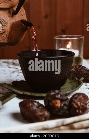 Serve tè saporito e fragrante in tazza di teiera in argilla e dolce datteri su vassoio bianco decorato con foglie di tè su legno sfondo Foto Stock