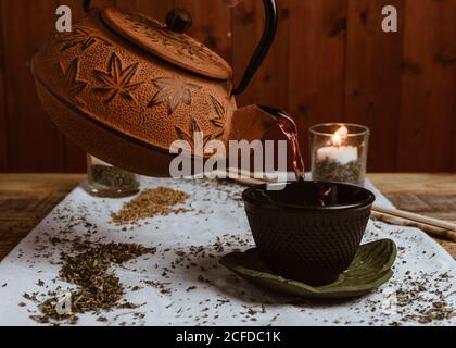 Serve tè saporito e fragrante in tazza di teiera in argilla e dolce datteri su vassoio bianco decorato con foglie di tè su legno sfondo Foto Stock