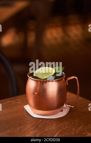 Classico cocktail alcolico Mosca Mule a base di vodka con zenzero birra e succo di lime serviti in tazza di rame decorata con fetta di limone su tavolo di legno Foto Stock