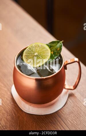 Dall'alto classico cocktail alcolico Mosca Mule a base di vodka con birra allo zenzero e succo di lime serviti in tazza di rame decorata con una fetta di limone su un tavolo di legno Foto Stock