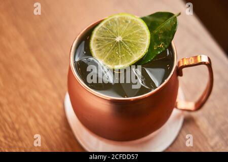 Dall'alto classico cocktail alcolico Mosca Mule a base di vodka con birra allo zenzero e succo di lime serviti in tazza di rame decorata con una fetta di limone su un tavolo di legno Foto Stock