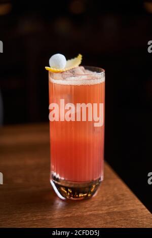 Bicchiere di cocktail Garibaldi rosso con succo d'arancia e. cubetti di ghiaccio decorati con scorza arancione su bancone di legno con sfondo nero Foto Stock