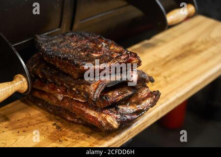 Composta pila di succulente costolette grigliate sul tagliere vicino barbecue Foto Stock