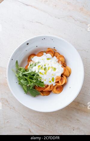 Vista dall'alto di gnocchi fritti in ciotola di ceramica bianca servita con panna acida e verde fresco nel ristorante Foto Stock
