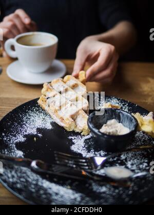 Piatto con resti di waffle e gelato tavolo da caffetteria vicino a una persona irriconoscibile che beve caffè Foto Stock