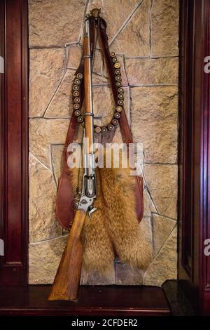 Fucile da caccia e cartuccia appesi con borsa in pelle e pelliccia pelts in legno telaio su muro di pietra Foto Stock