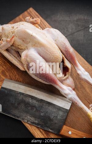 Da sopra scissione shabby e pollo intero crudo posto sopra tagliere in legno in cucina Foto Stock