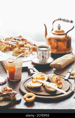 Tazza e teiera di rame di tè caldo messo sul tavolo tra torta e toast con albicocche e marmellata a casa Foto Stock