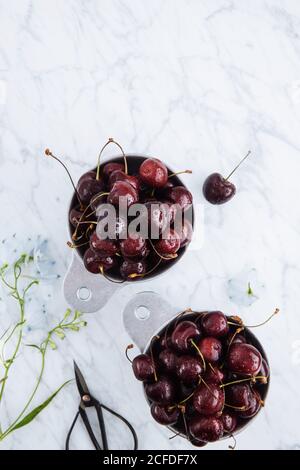 Vista dall'alto delle pentole con ciliegie rosse dolci mature con tavolo in marmo con ramo verde Foto Stock