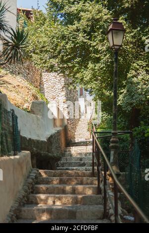 Atmosfera pomeridiana. Calmo, tranquillo, accogliente scala in pietra e muro, lampada su una colonna di ghisa, e lussureggiante fogliame nel parco della città vecchia. Foto Stock