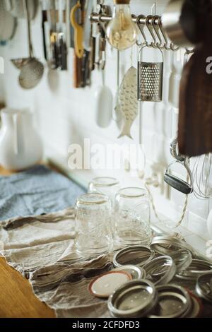 Vasetti di vetro lavati e coperchi di metallo preparati per inscatolamento e. conservando posto sul tavolo in cucina domestica con gli utensili Foto Stock