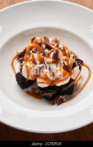 Dall'alto di fette di brownie con gelato bianco e pezzi di cioccolato serviti con caramello su piatto bianco Foto Stock