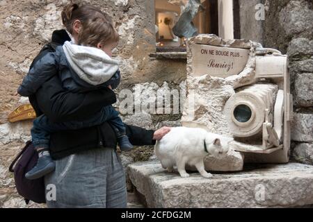 Saint-Paul-de-Vence non toccare la statua, piuttosto stropiccare il gattino! Giovane madre con bambino tra le braccia. La statua della macchina fotografica di Luc Trizan, gatto bianco. Foto Stock