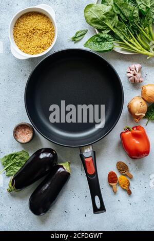 Dall'alto vengono organizzate varie verdure e spezie per la preparazione del pranzo intorno a padella vuota sul tavolo in cucina Foto Stock