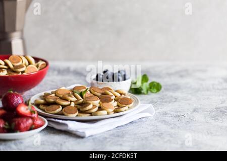 Minuscoli pancake per colazione. Frittelle di cereali con mirtilli, banane, fragole su sfondo grigio. Cibo alla moda. Spazio di copia per testo o disegno Foto Stock