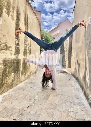 Handstand con una mano, giovane donna, città vecchia, vicoli, cielo blu, pavimento in pietra, estate, joie de vivre, forza, vacanza, pazzo, overhead, Foto Stock