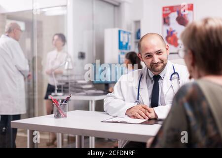 Medico con paziente anziano durante l'esame medico in ospedale che indossa cappotto bianco e stetoscopio. Medico maturo che discute la diagnosi con la giovane donna malata sul corridoio della clinica Foto Stock