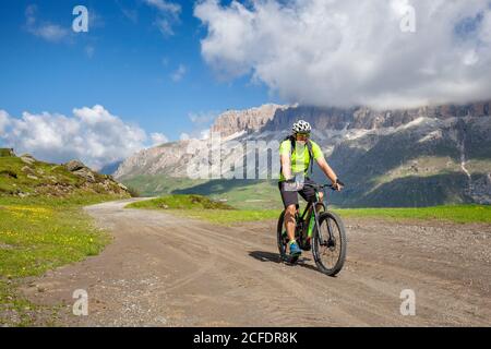 Ciclista con una mountain bike elettrica (e-bike) lungo il sentiero Viel del Pan (Bindelweg) di fronte al gruppo del Sella, ai confini tra il Veneto Foto Stock